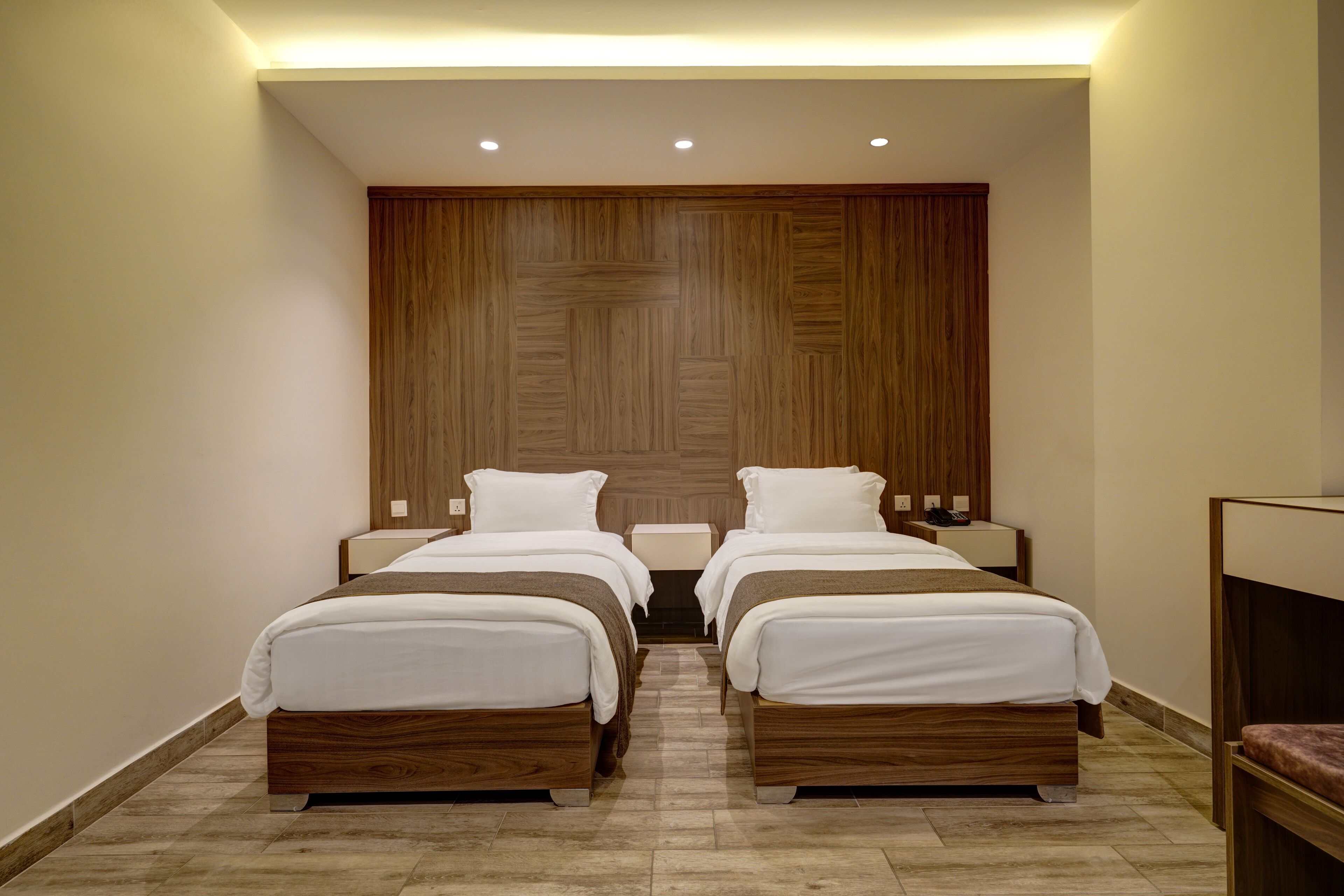 Une chambre d’hôtel avec deux lits simples, une tête de lit en bois, une table de chevet et un petit coin salon.