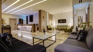 Een moderne hotellobby met een receptiebalie, zithoeken en een televisiescherm.