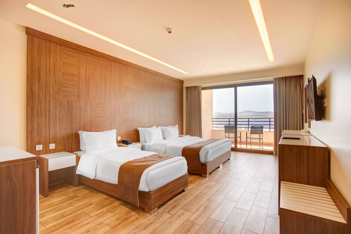 Une chambre d’hôtel avec deux lits, un bureau, une télévision et un balcon avec vue.