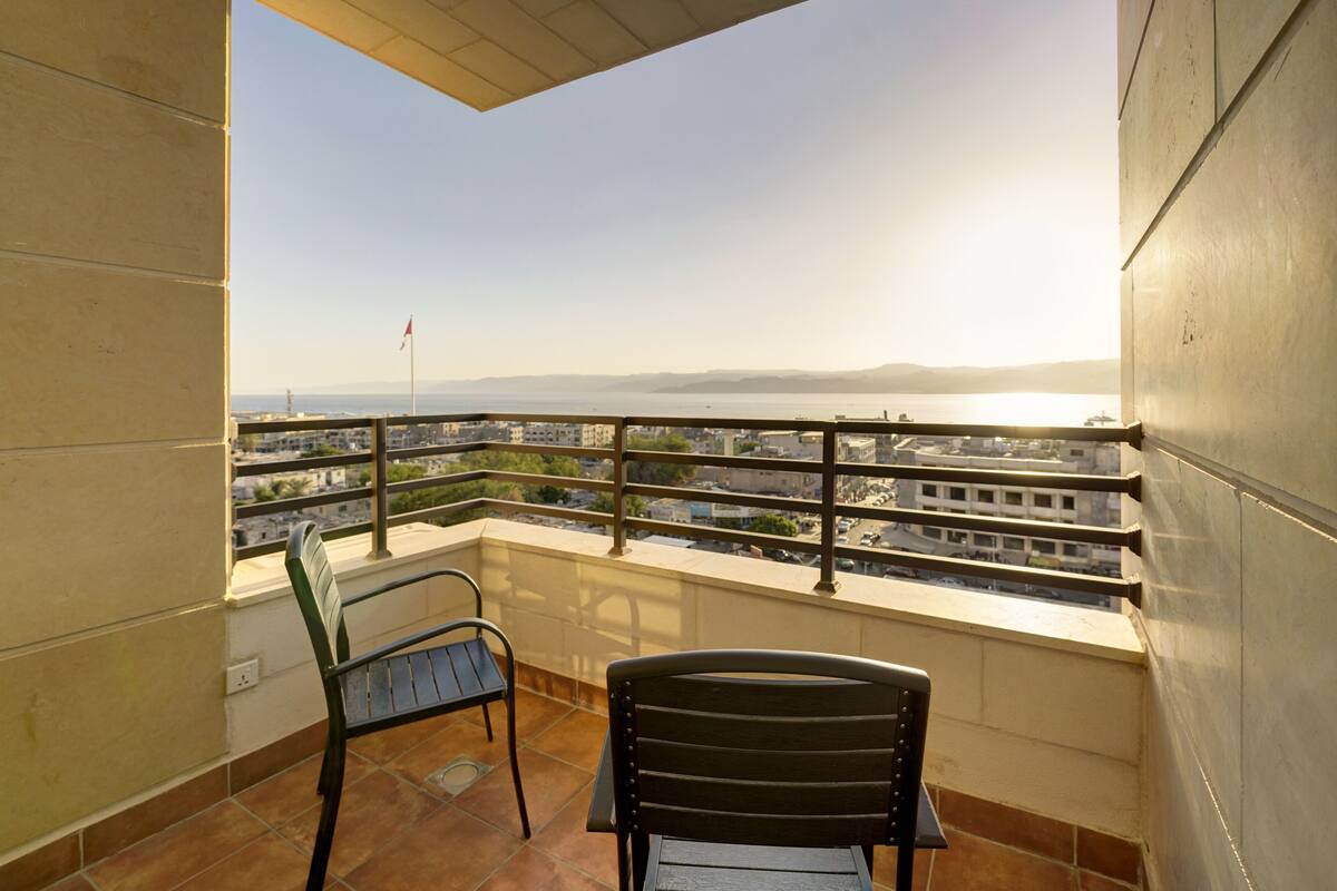 Un balcon avec deux chaises, une vue sur le paysage urbain et un ciel dégagé.