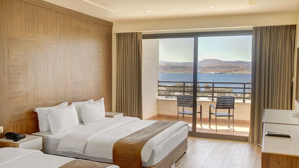 Een hotelkamer met twee bedden, een balkon met uitzicht op zee en een bureau met telefoon.