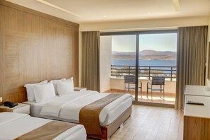Een hotelkamer met twee bedden, een balkon met uitzicht op zee en een bureau met telefoon.