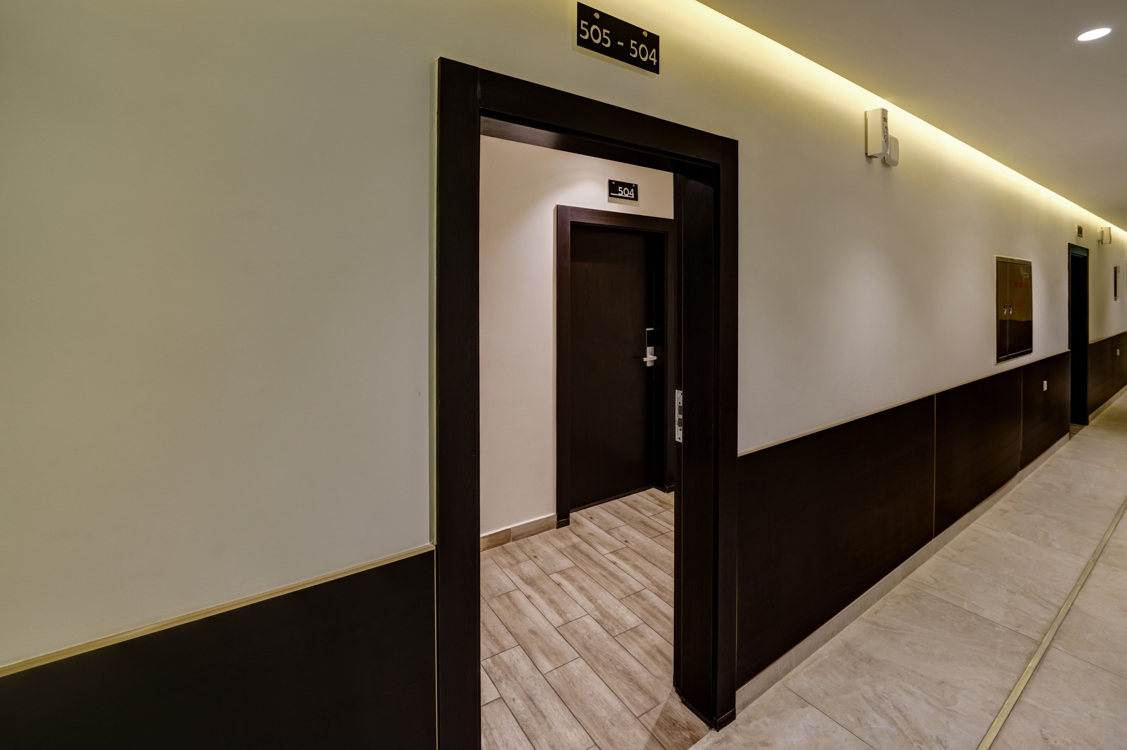 Un couloir avec une signalétique indiquant les numéros de chambre 505 et 504, une porte et un luminaire fixé au mur.