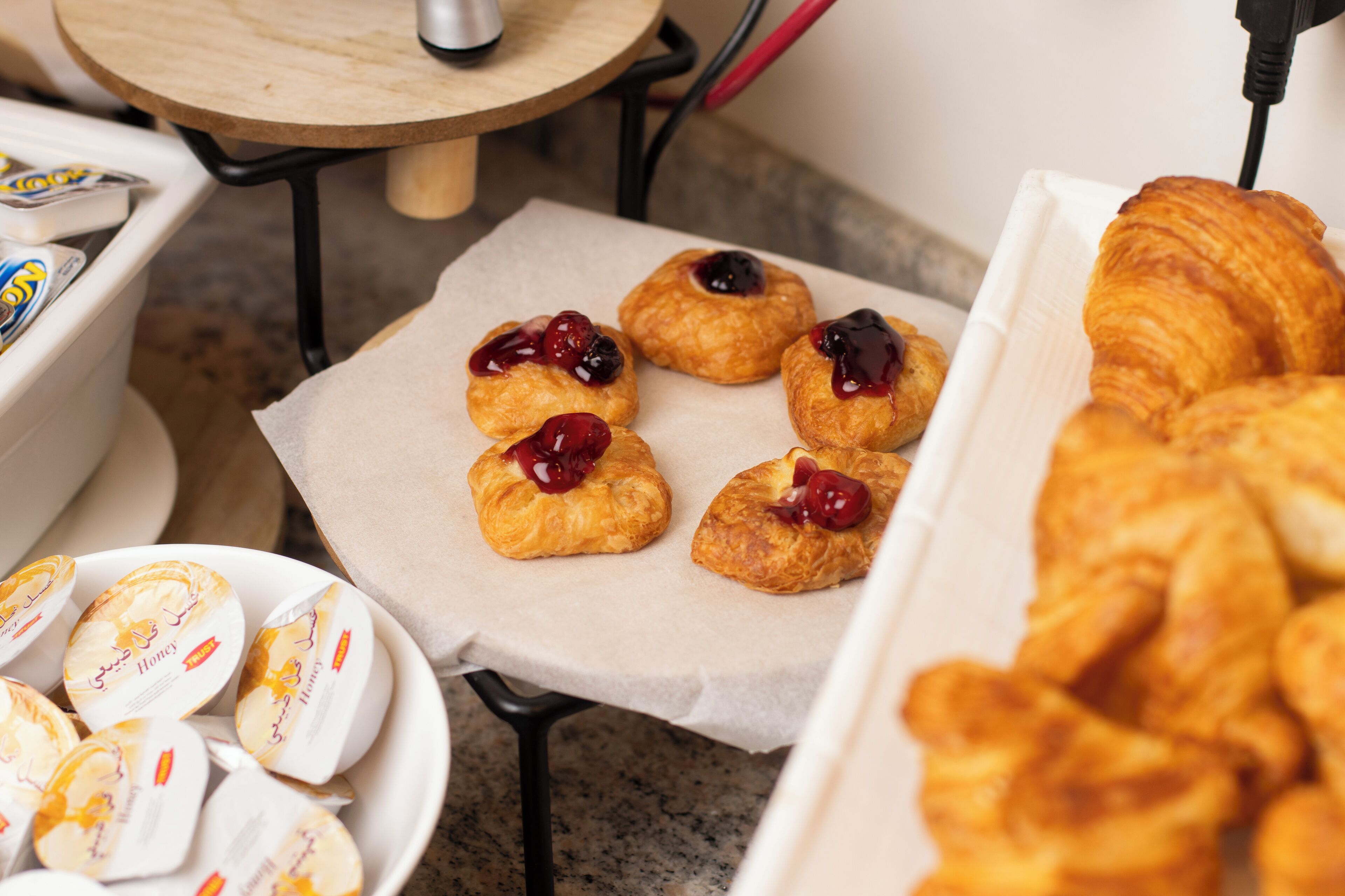 Taula amb pastissos, incloent croissants i pastissos amb melmelada, i un recipient d'aperitius amb sabor de mel.