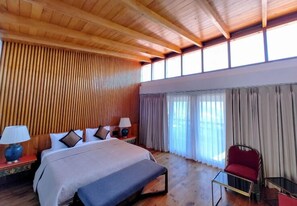 A hotel room with a wooden ceiling, a bed with pillows and a bench, a red chair, and a small table.