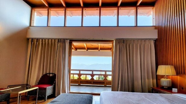 Hotelkamer met een groot bed, een stoel, een tafeltje en uitzicht op de bergen vanuit een balkon.