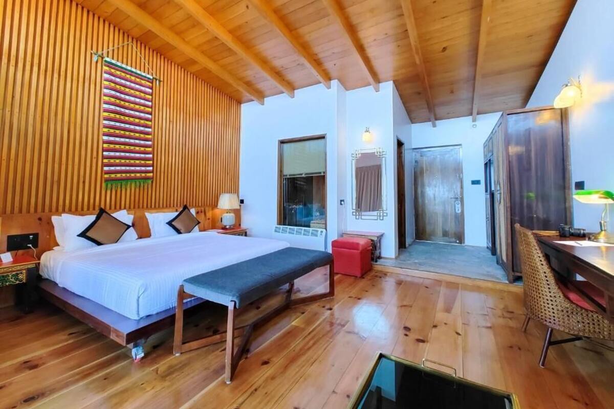A wooden-floored bedroom with a bed, bedside table, bench, and a dining area with a table and chairs.