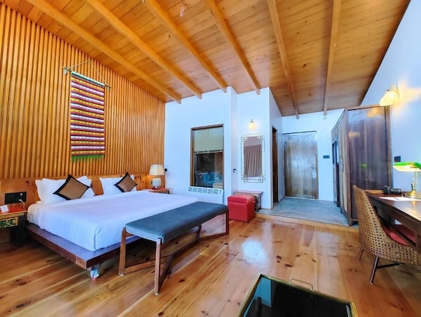 A wooden-floored bedroom with a bed, bedside table, bench, and a dining area with a table and chairs.