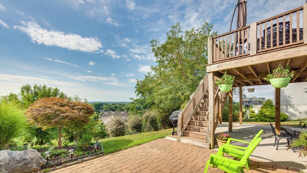 A patio with brick flooring, green chairs, a wooden deck with a railing, and hanging planters.