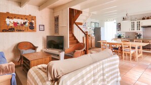 Un'ampia zona giorno con divano, televisione e tavolo da pranzo con sedie. Una scala conduce a un livello superiore.