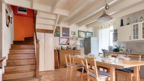 Una cucina con mobili in legno, un tavolo da pranzo con sedie e una scala che conduce a un'altra stanza.