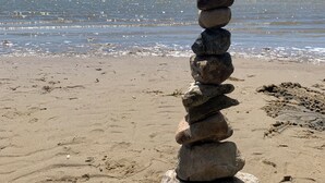 En hög med stenar på en sandstrand, med ett lugnt hav i bakgrunden.