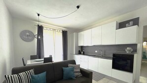 A modern kitchen with white cabinets, a built-in oven, and a dining area with a table and chairs. - Affittimoderni La Maddalena - MADA19 (La Maddalena)
