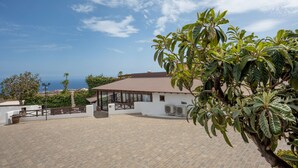 Um edifício branco com telhado castanho, um pátio pavimentado e vista para o mar.