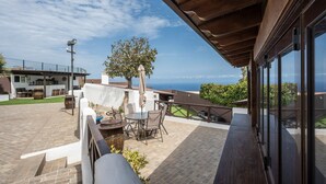 Um pátio com mesa e cadeiras, uma árvore e vista para o oceano.