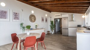 Cozinha moderna com vigas de madeira, área de refeições com cadeiras vermelhas e uma geladeira.