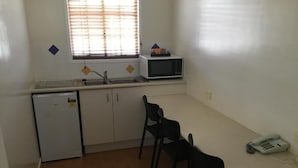 Eine kompakte Küche mit Kühlschrank, Mikrowelle, Spüle und einer kleinen Essecke mit Stühlen.