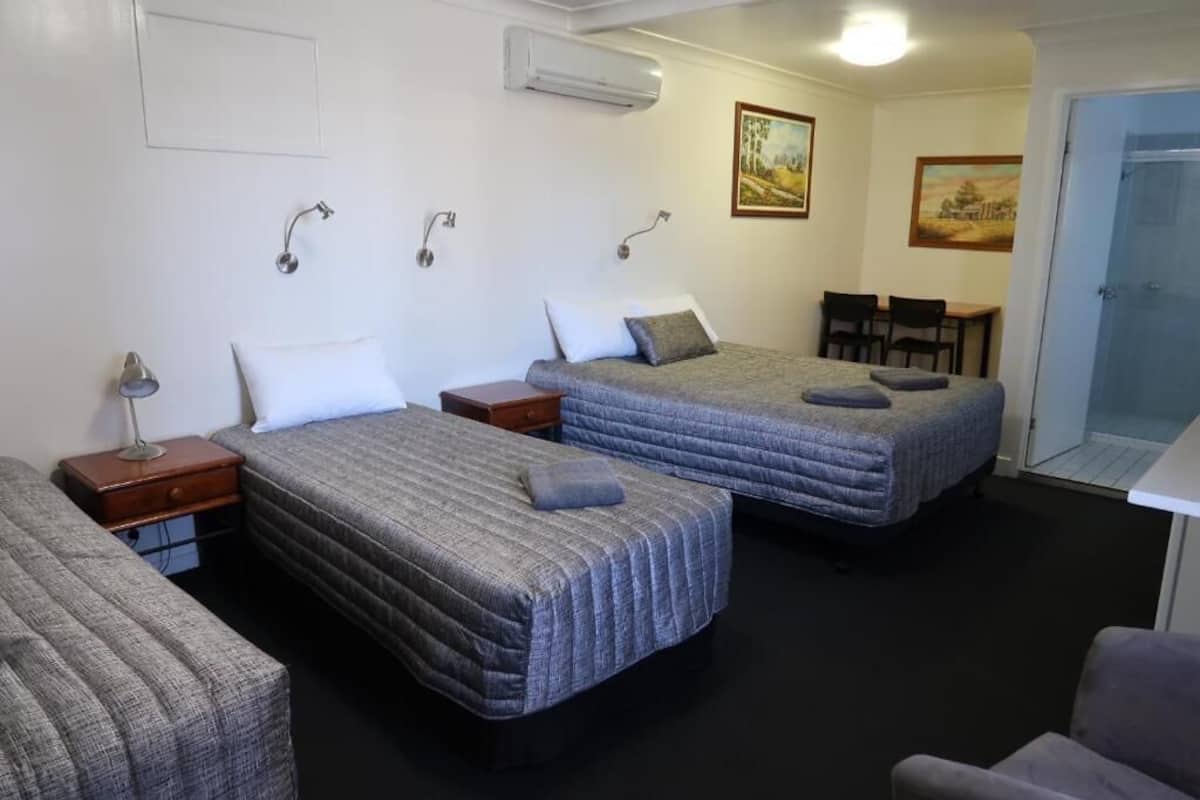 A room with two beds, a desk, and a chair. There are wall-mounted lights and an air conditioning unit.