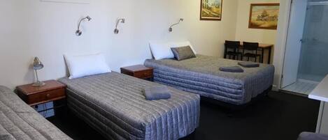 A room with two beds, a desk, and a chair. There are wall-mounted lights and an air conditioning unit.