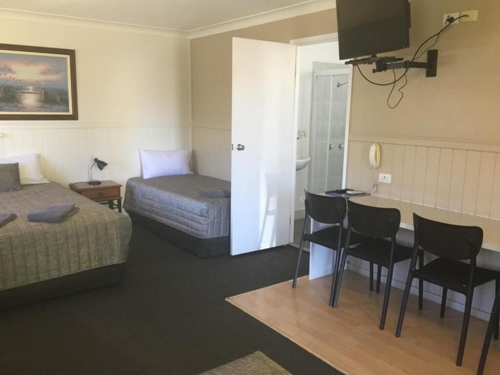 A room with a bed, a desk with two chairs, a television mounted on the wall, and a bathroom door.