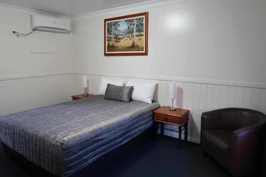 A bedroom with a bed, nightstands, a chair, and a wall-mounted air conditioner.