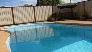 Ein rechteckiger Pool mit Fliesenrand, umgeben von einer Ziegelterrasse und einem Metallzaun.