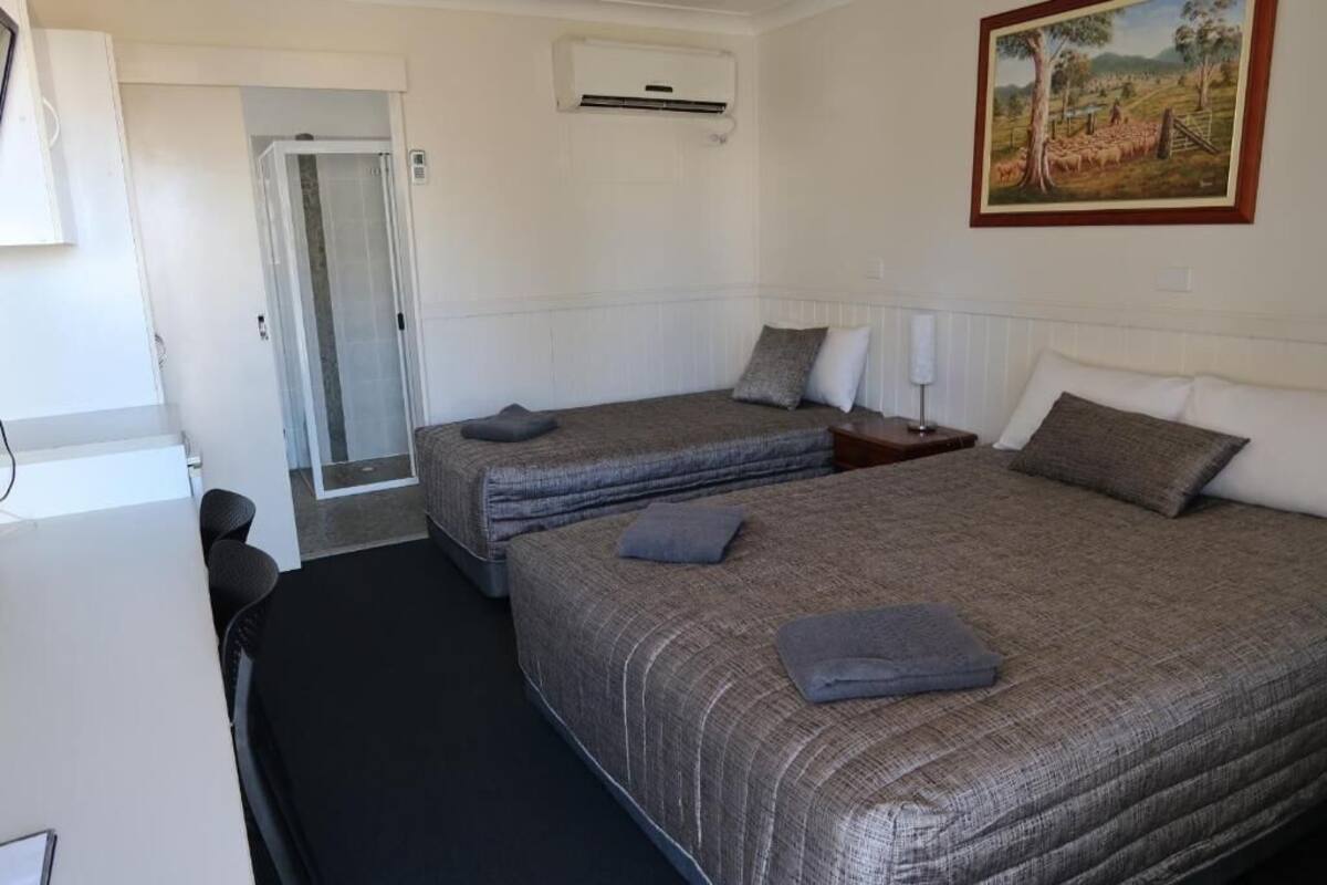 A hotel room with two beds, a door, an air conditioning unit, and a painting on the wall.