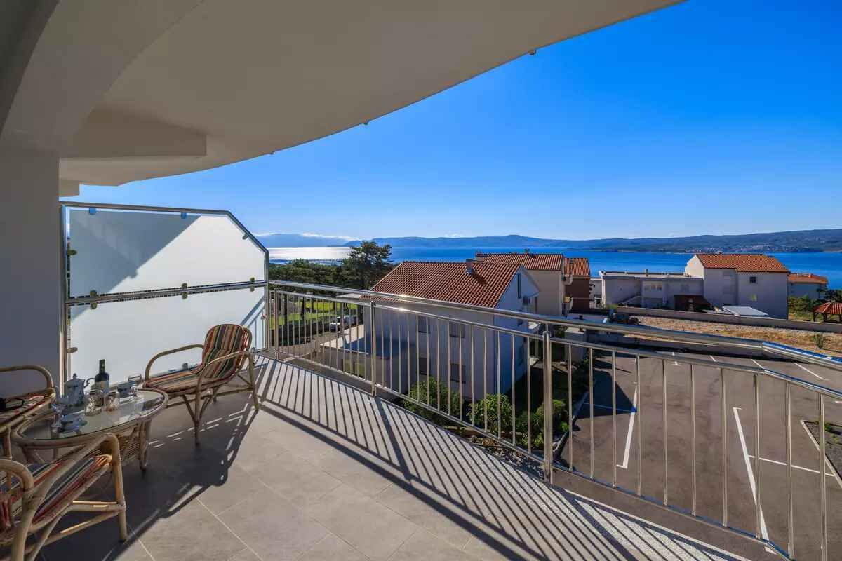 A balcony with a view of the sea, a dining table, and chairs.