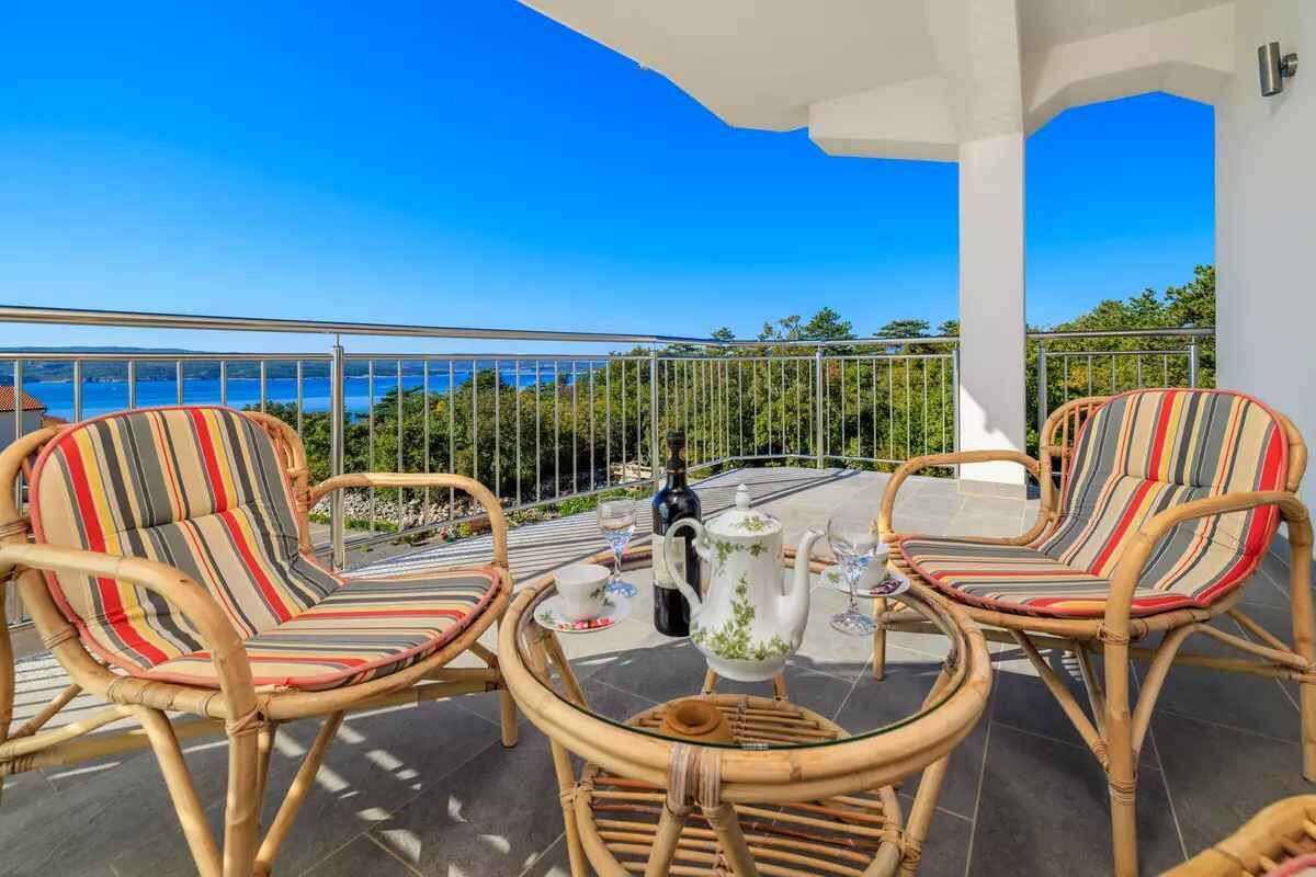 Ein Balkon mit Korbmöbeln, einem Tisch mit Teekanne und Gläsern sowie Blick aufs Meer.