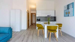 A modern kitchen with white cabinets, a dining table with yellow chairs, and a blue sofa in a bright room with wooden flooring.