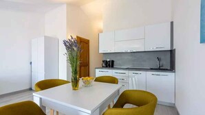 A modern kitchen with white cabinets, a white countertop, and a built-in oven. There is a dining table with four mustard-colored chairs and a vase with flowers on it.