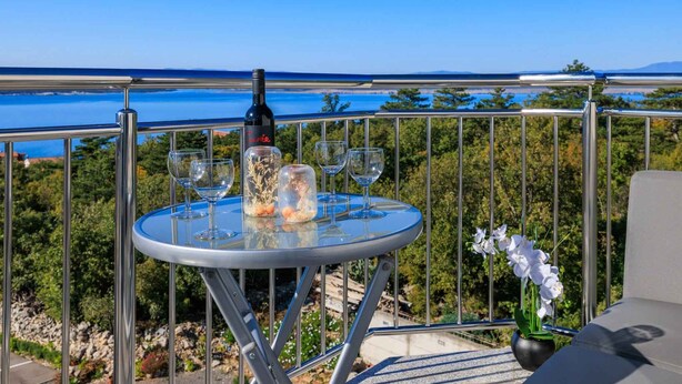 Ein Balkon mit Tisch für Zwei, einer Weinflasche und einem Blumenstrauß.
