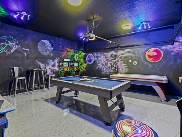 A pool table with a pool cue, two chairs, and a table with a drink dispenser. - Waterpark Enclave with Epic Game Room! Prvt Movie Theatre! Themed Luxury! (Davenport)