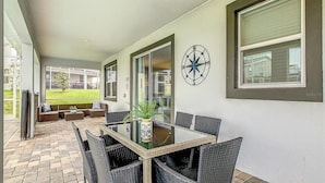 A covered patio with a dining table and chairs, a clock on the wall, and a view of the outside. - Waterpark Enclave with Epic Game Room! Prvt Movie Theatre! Themed Luxury! (Davenport)
