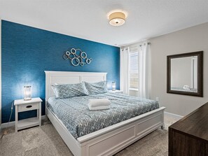 A bedroom with a bed, nightstands, a mirror, and a blue accent wall. - Waterpark Enclave with Epic Game Room! Prvt Movie Theatre! Themed Luxury! (Davenport)