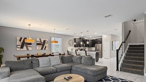 A modern living room with a sectional sofa, a coffee table, and a dining area with a chandelier. - Waterpark Enclave with Epic Game Room! Prvt Movie Theatre! Themed Luxury! (Davenport)