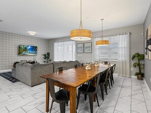 A modern living room with a wooden dining table, grey sofa, and a TV on the wall. - Waterpark Enclave with Epic Game Room! Prvt Movie Theatre! Themed Luxury! (Davenport)