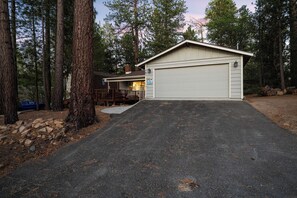 A garage with a covered driveway leading to a house, surrounded by tall trees.