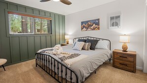A bedroom with a bed, nightstands, a window with blinds, a ceiling fan, and a wall-mounted air conditioner.