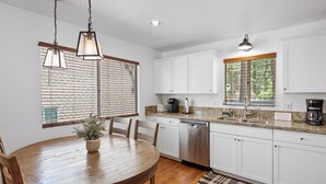 A modern kitchen with white cabinets, a wooden dining table, and pendant lights.