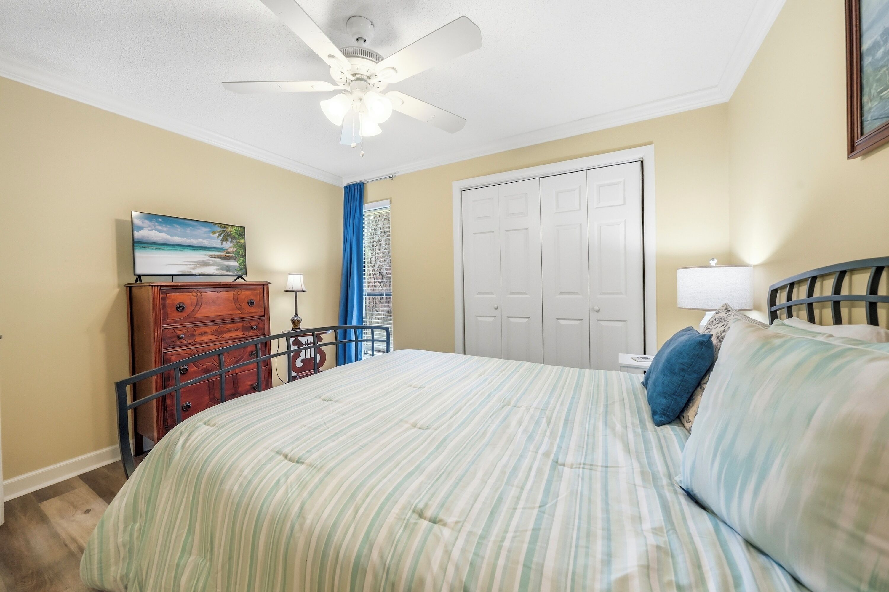 A bedroom with a bed, a dresser, a ceiling fan, a door, and a window with curtains.