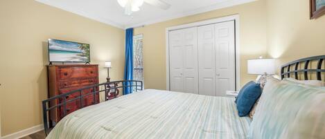 A bedroom with a bed, a dresser, a ceiling fan, a door, and a window with curtains.