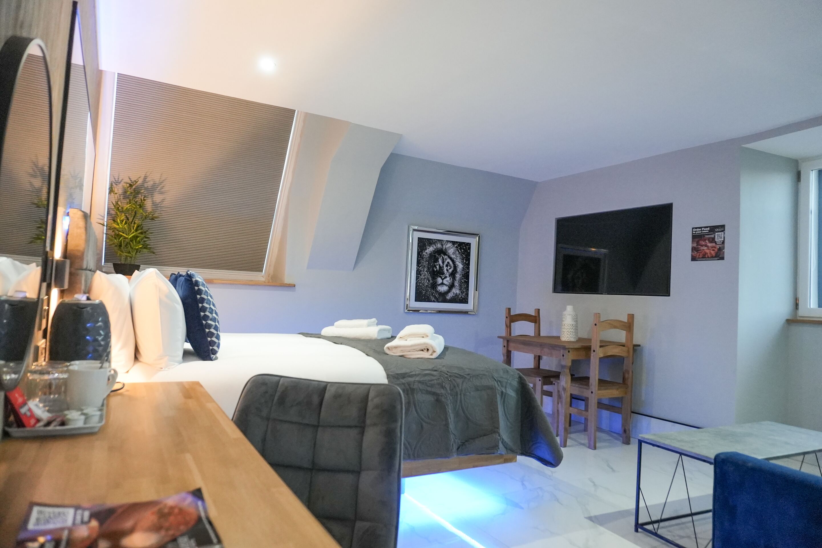 Una habitación de hotel moderna con cama, mesita de noche, escritorio, silla y televisor en la pared.