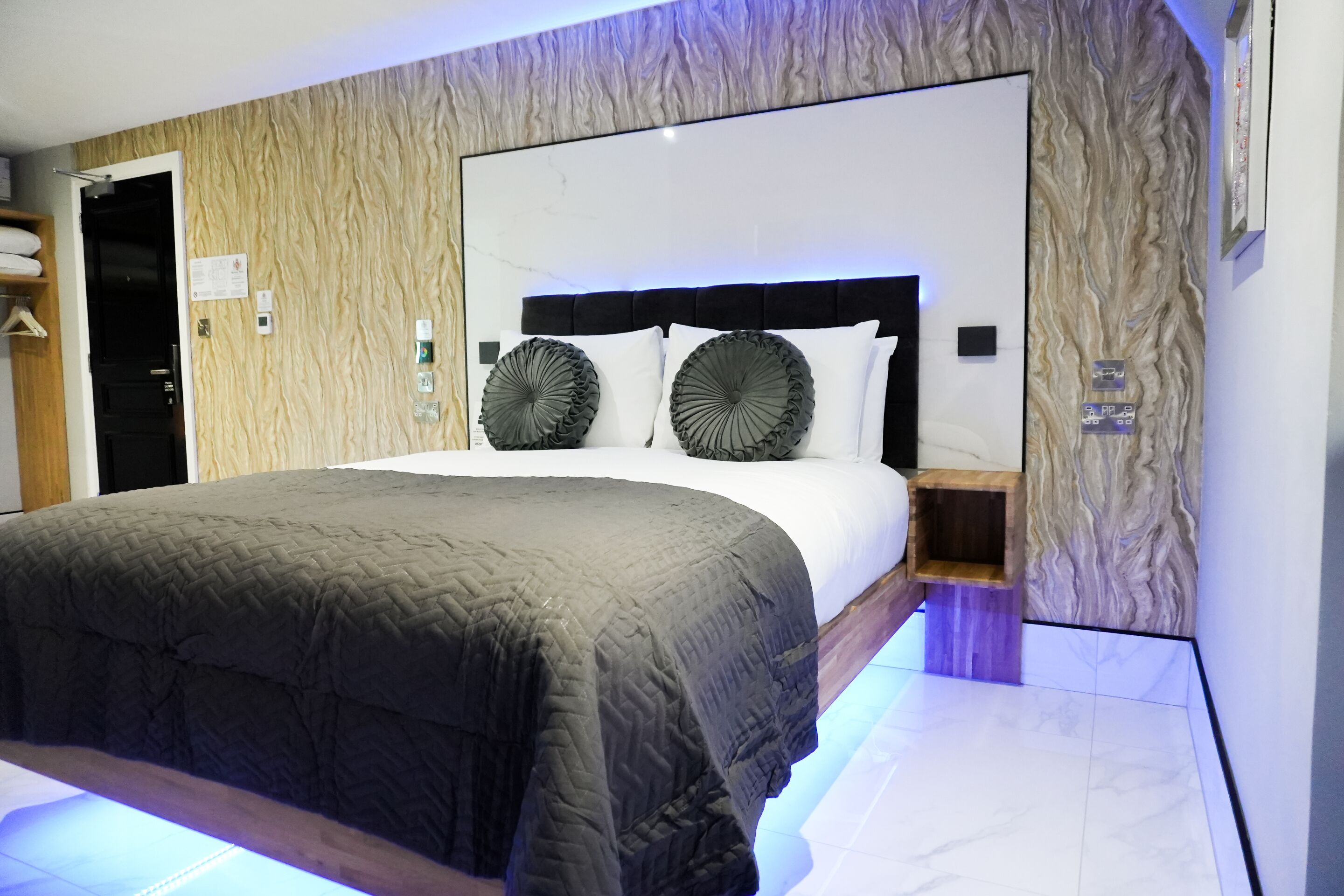 A modern bedroom with a large bed, a headboard with built-in lighting, and a wooden panel wall design.