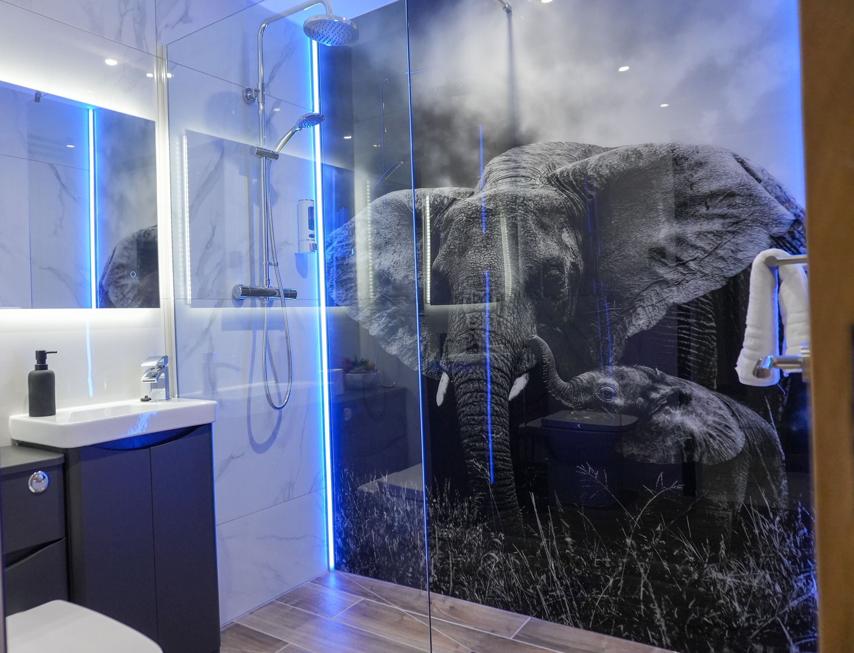 Ein modernes Badezimmer mit Duschkabine aus Glas, Waschtisch mit Marmorplatten und einer großen Elefanten-Mural.