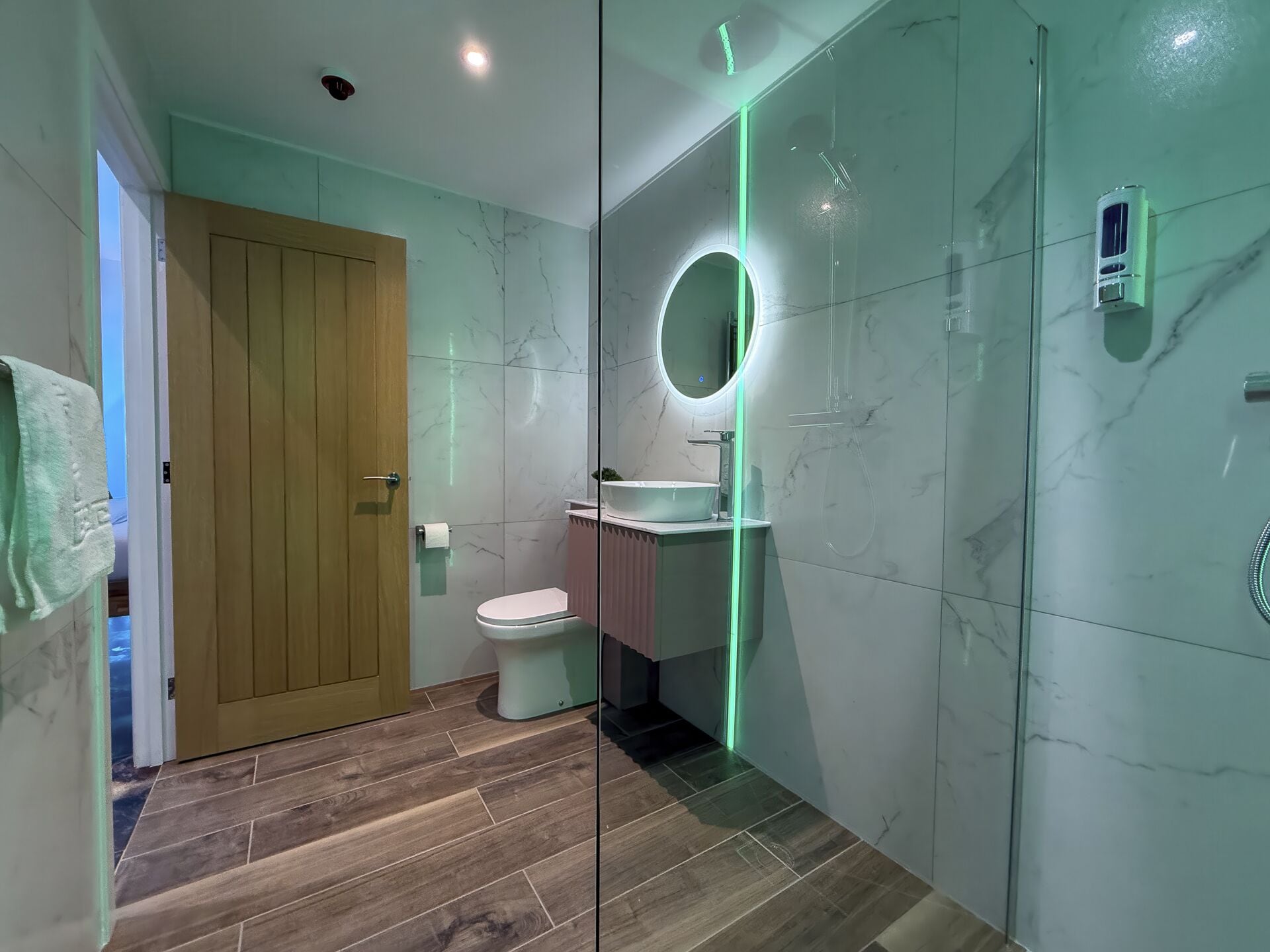 A modern bathroom with a wooden door, a toilet, a sink with a mirror, and a shower area.
