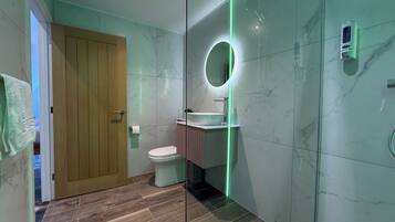 A modern bathroom with a wooden door, a toilet, a sink with a mirror, and a shower area.