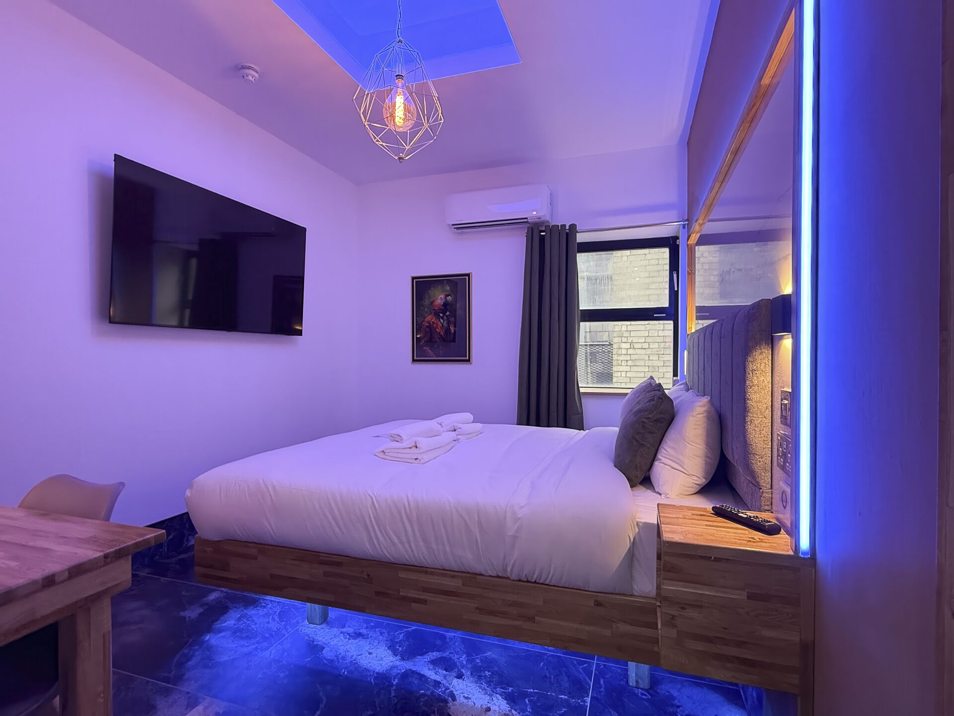 Un dormitorio moderno con cama, televisor montado, un cuadro y una ventana con cortinas.