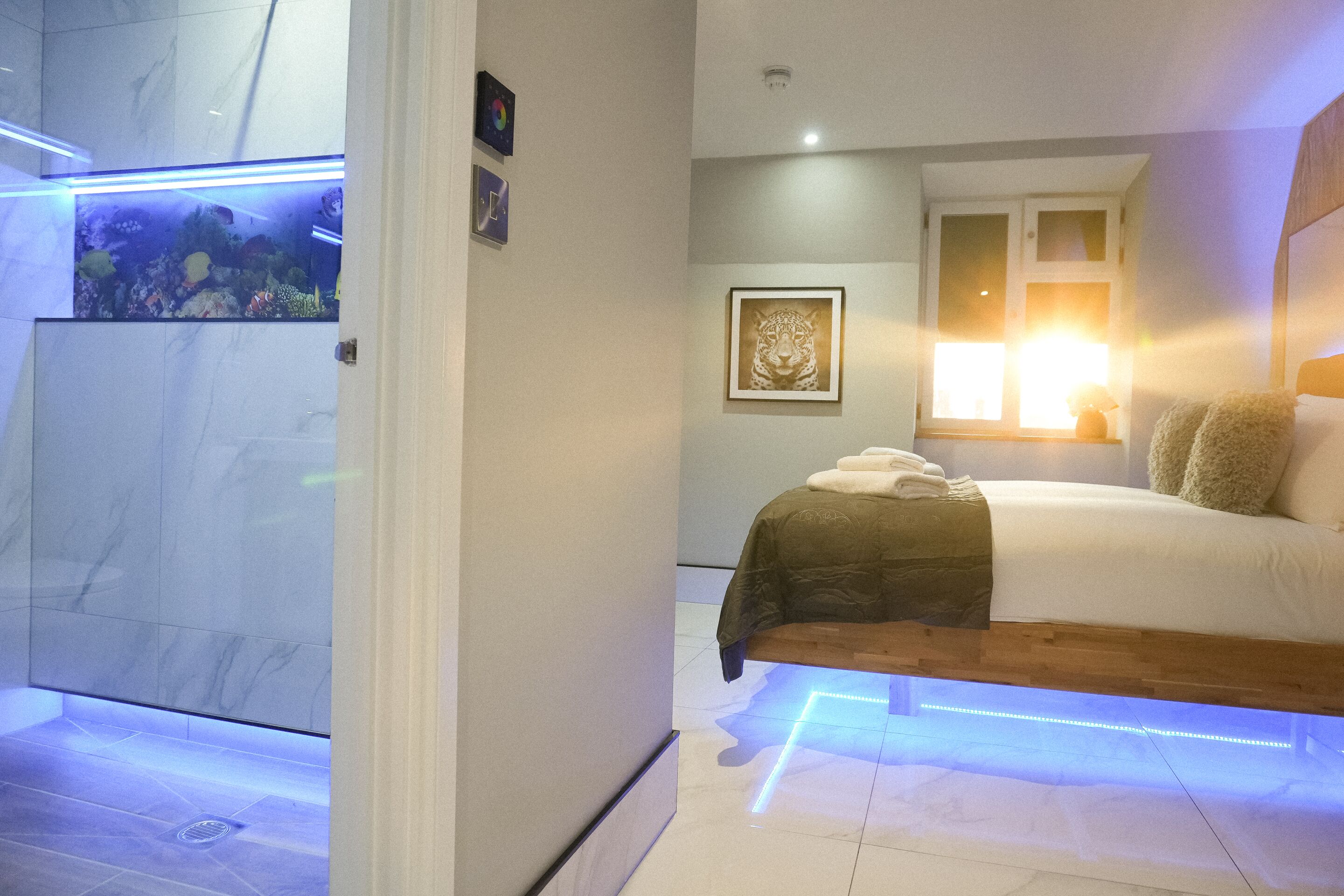 A modern bedroom with a bed, a nightstand, a wall-mounted aquarium, and a framed artwork.