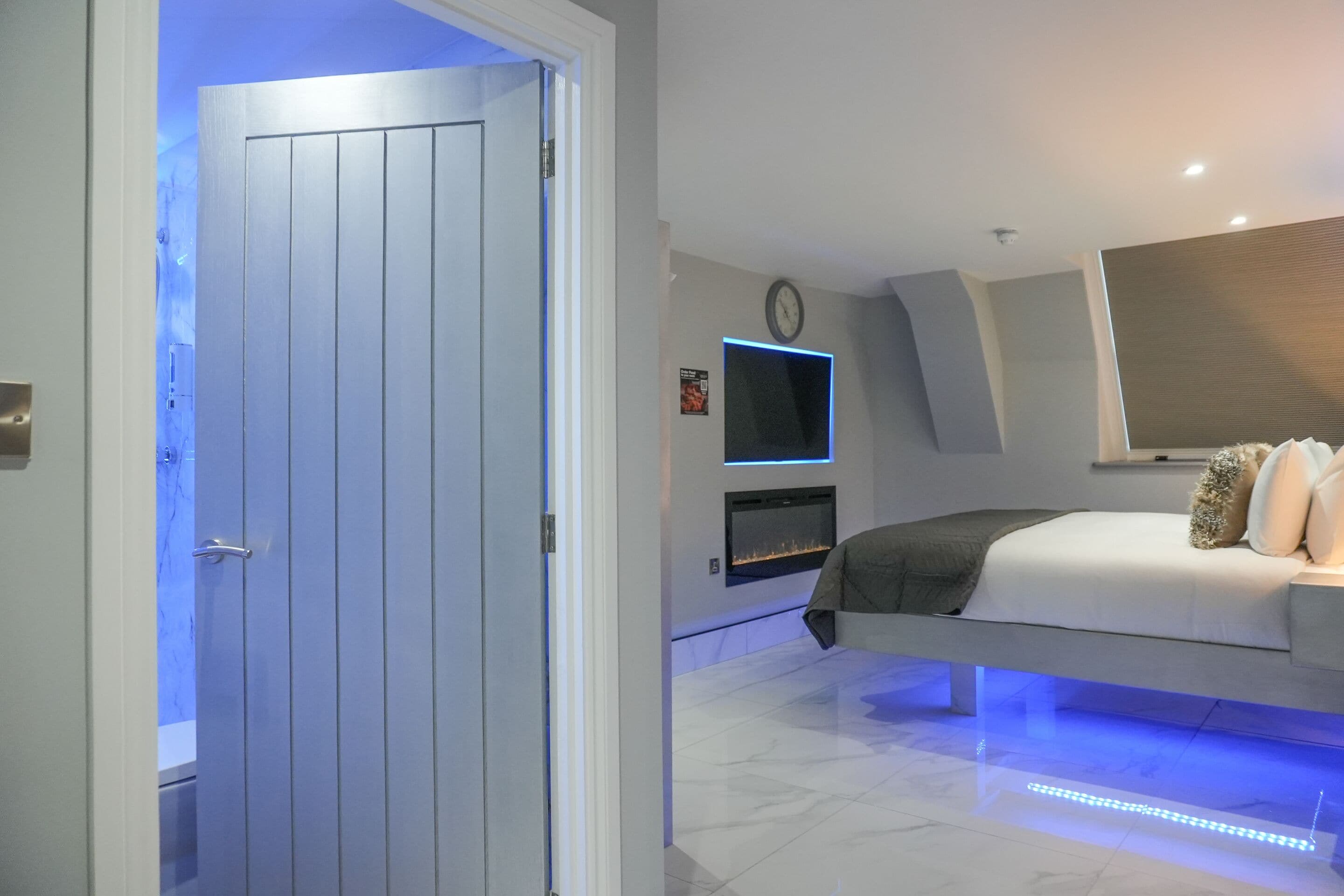 A modern bedroom with a bed, a TV mounted on the wall, and a fireplace.